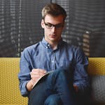 Person in Blue Denim Jacket Sitting on Chair While Writing